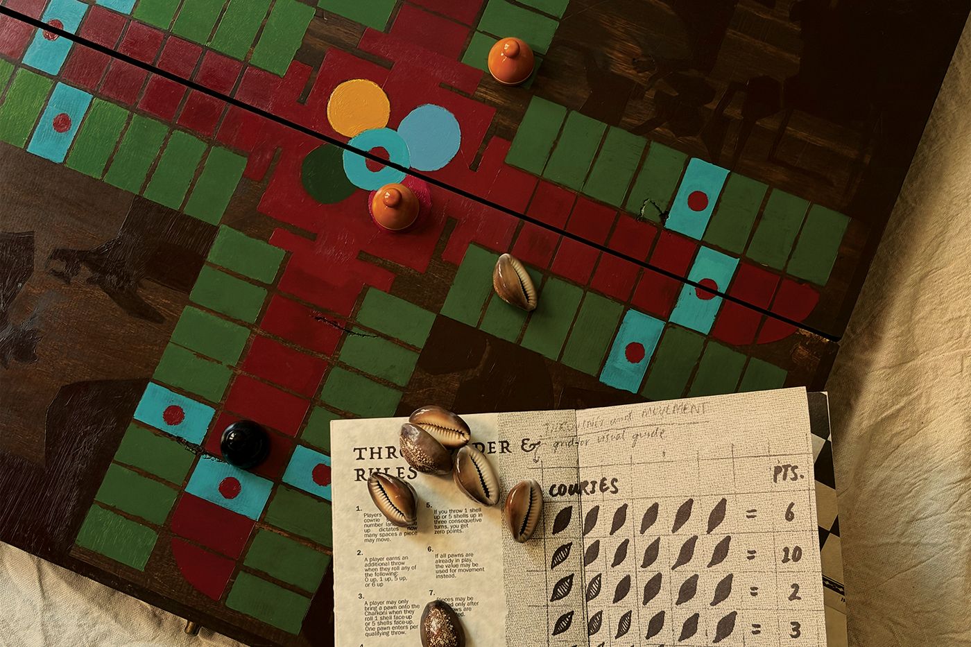 Pachisi Reimagined game board with cowrie shells and an open rules guide.