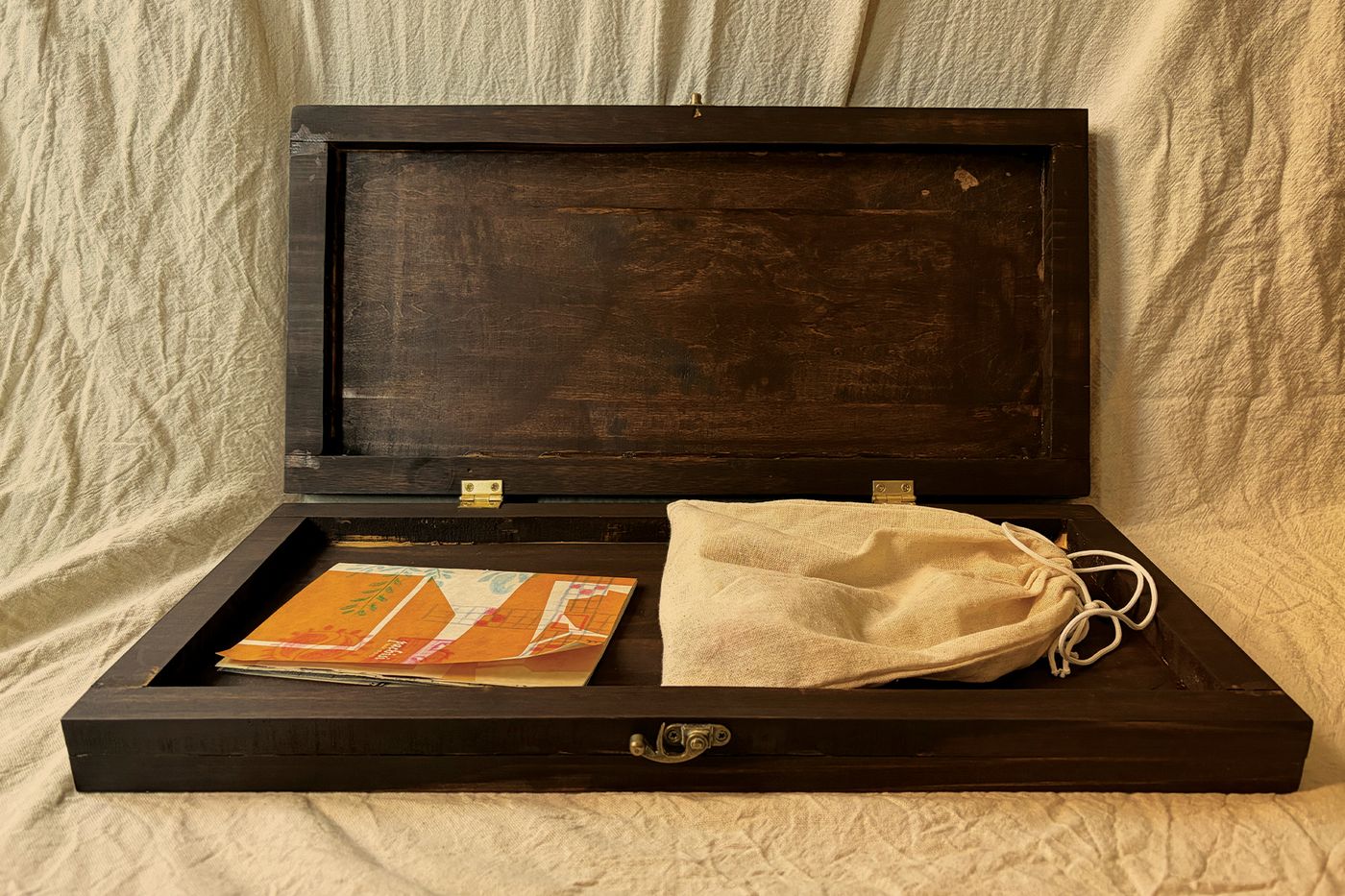 Pachisi Reimagined wooden game box open with the rulebook and drawstring pouch inside.